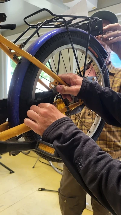 Close-up of two hands fixing the fender and luggage rack of a children's bicycle.