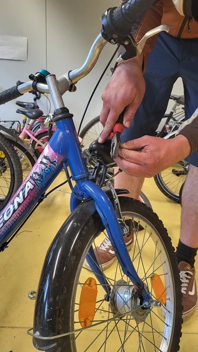 Eine Person schneidet mit einer Zange ein Bremsseil an einem blauen Kinderfahrrad zurecht.