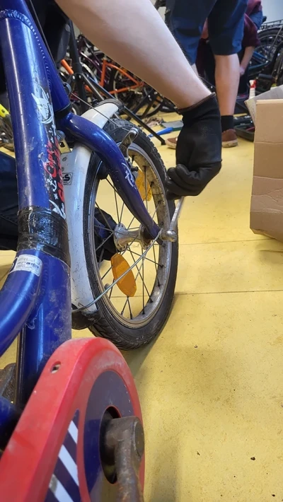 A person is repairing the rear wheel of a small children's bike with training wheels.